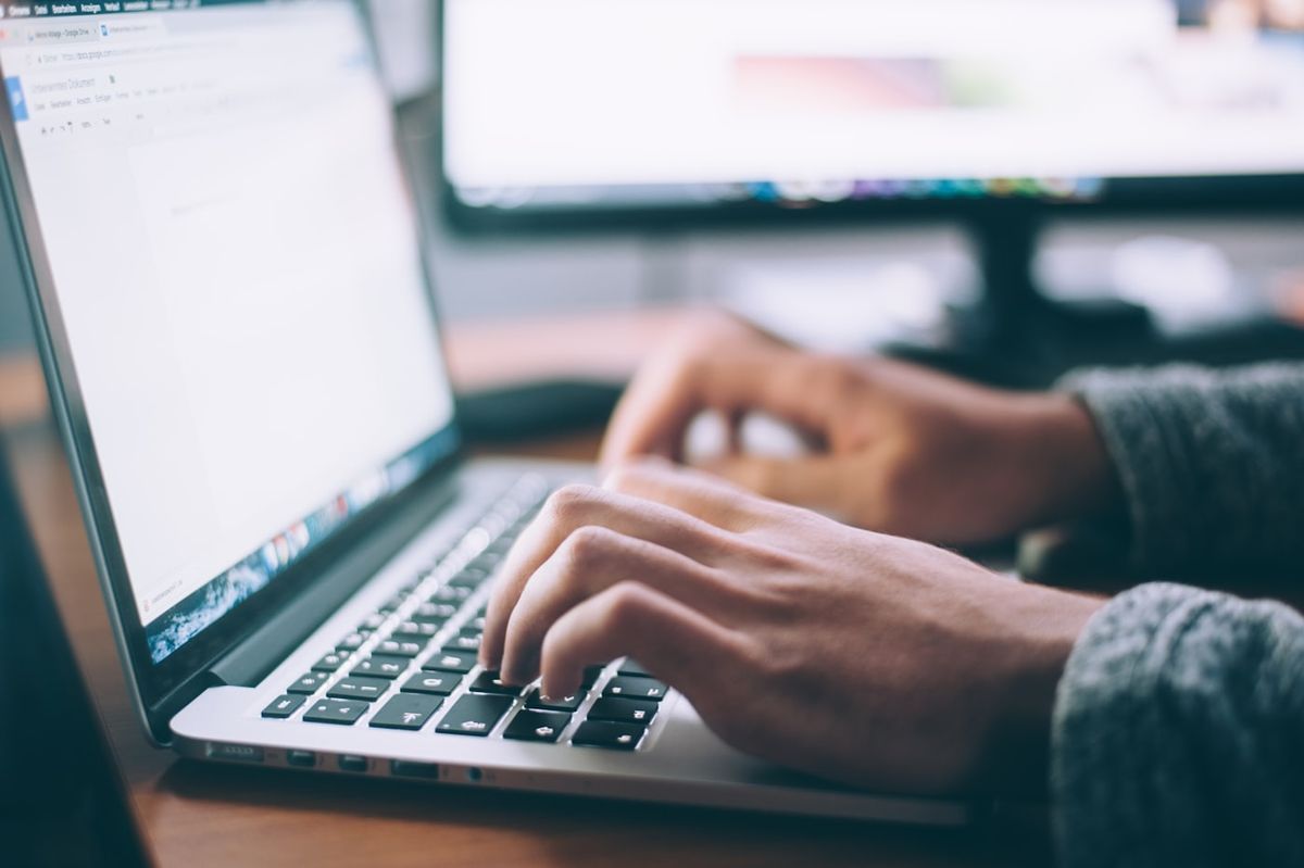 Person arbejder paa baerbar computer ved et skrivebord