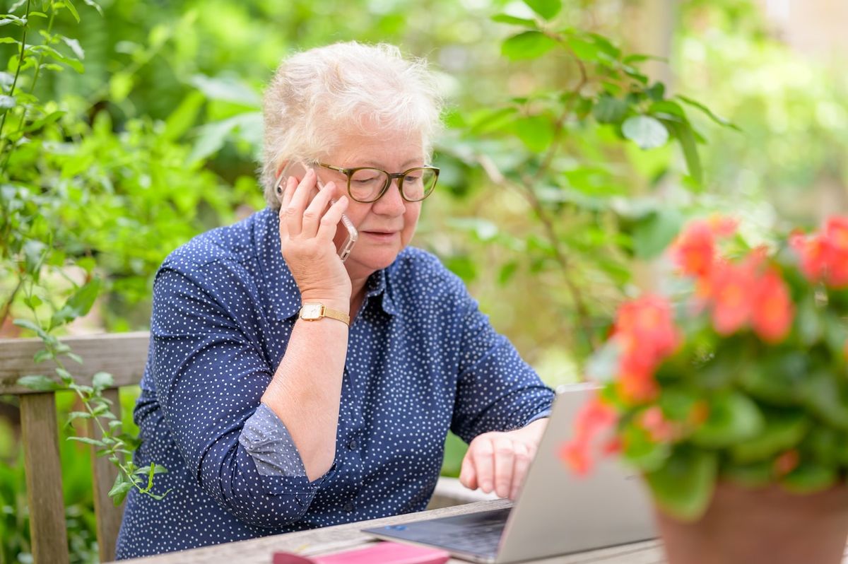 Ældre kvinde sidder ved en bærbar computer og taler i telefon for at få hjælp